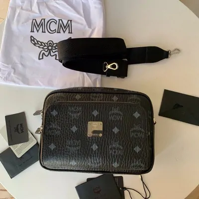 A dark monogrammed crossbody bag with a wide detachable strap, resting on a white cloth