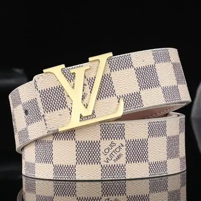 A checkered cream and grey belt coiled on a pale surface, fitted with a large flat gold buckle