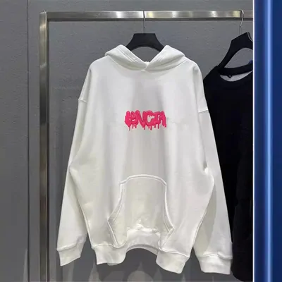 A white pullover hoodie with a small pink chest print, hanging open on a rail
