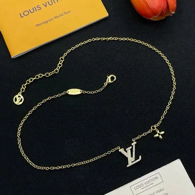 A fine gold-tone chain bracelet with a small engraved tag, arranged on a black surface beside a yellow box