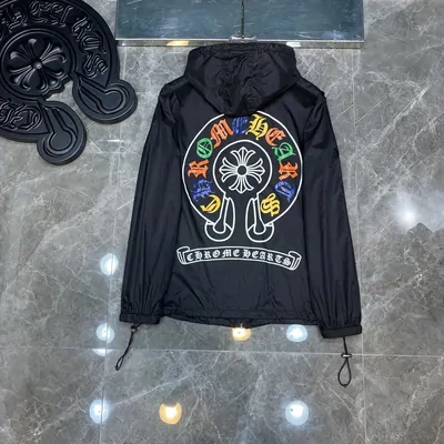 A black hooded windbreaker laid flat on grey stone, printed with a round multicoloured graphic across the back