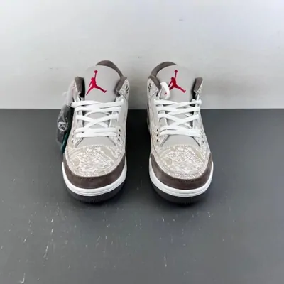 A pair of low-top sneakers in grey and white with patterned side panels, photographed straight on against a plain floor
