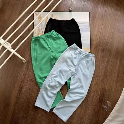 Three pairs of sweatpants in black, green and pale blue, laid out on a wooden floor